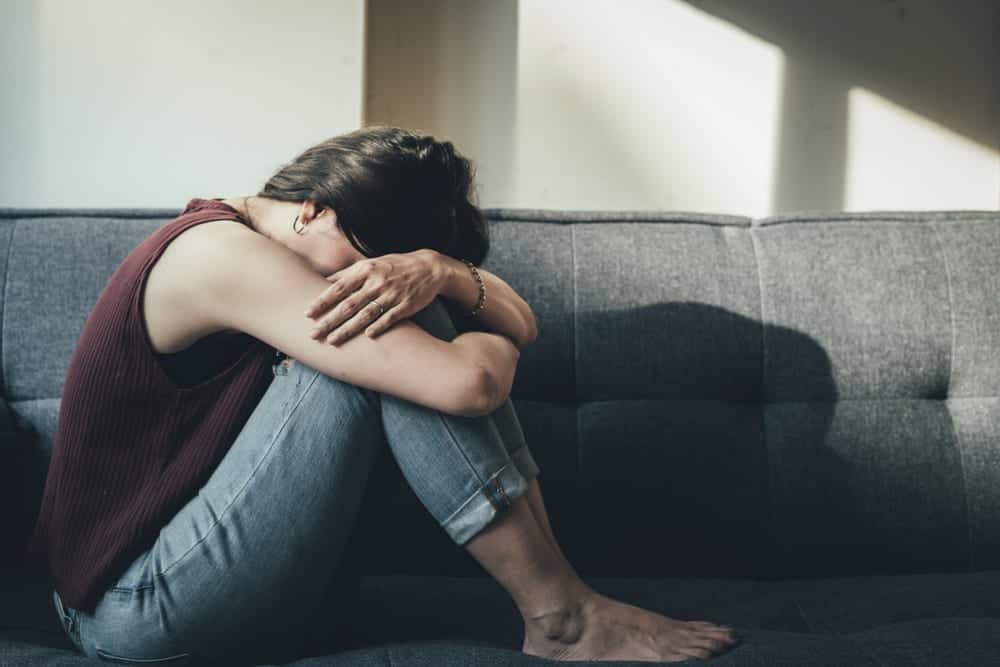 Anxious girl sitting on couch with head in arms