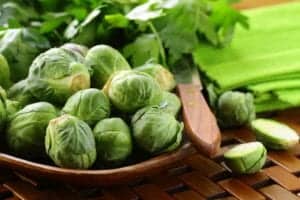 whole brussel sprouts in a brown bowl next to cut brussel sprouts and a green napkin