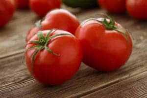 three red tomatoes on a wooden surface