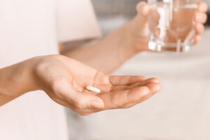 person holding a glass of water and their allergy pill